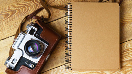 Old retro camera,  spiral blank kraft paper notebook on vintage rustic wooden planks boards. Education photography courses back to  school concept abstract background. Close up, top view, horizontal.