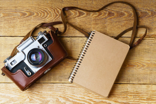 Old retro camera,  spiral blank kraft paper tablet on vintage rustic wooden planks boards. Education photography courses back to  school concept abstract background. Close up, top view, copy space.