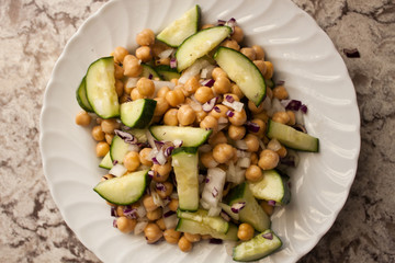Close Up Chickpea, Cucumber, and Red Onion Salad in White Bowl on Marble Countertop