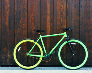 Bright green Fixed Gear beautiful vintage bicycle stands in a black wooden wall
