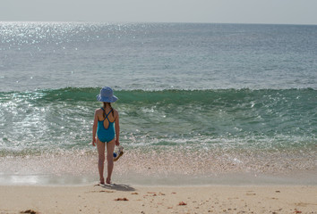 Girl in a swimsuit stands and looks at the ocean