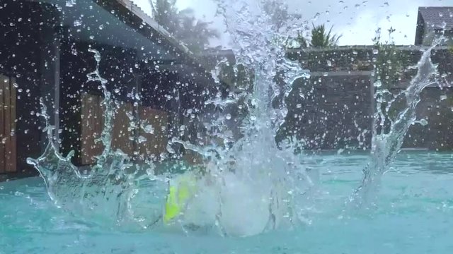 Slow motion footage of happy little boy splashing water in the swimming pool while wearing swimsuit and goggles
