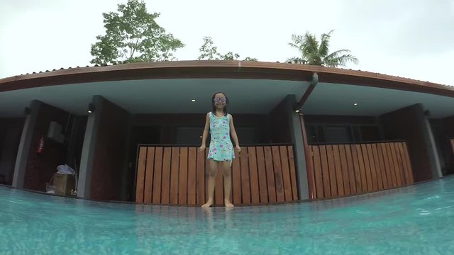 Slow motion footage of a cute little girl jumping into a swimming pool while wearing swimsuit and goggles