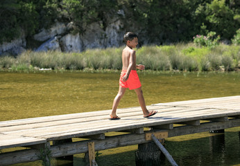 Boy walking on a wooden foot bridge on a lake