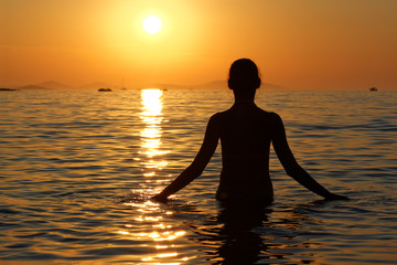Sylwetka kobiety w wodzie na tle zachodzącego słońca
