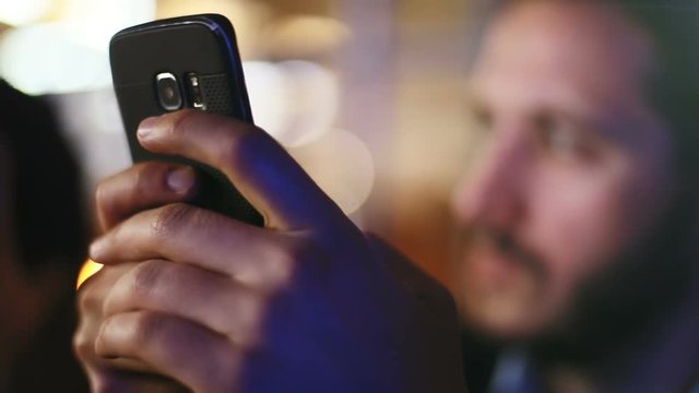 Young elegant bearded man using smartphone at party and smiling in camera
