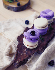 Obraz na płótnie Canvas Lavender violet macarons on table. Purple macaron cookies. Blackberry macarons on wooden plate and berries over grey texture background. Lavender cookie with berry.