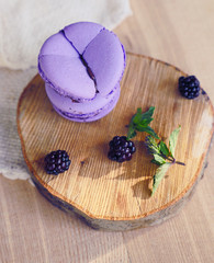 Lavender violet macarons on table. Purple macaron cookies. Blackberry macarons on wooden plate and berries over grey texture background. Lavender cookie with berry.
