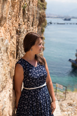 Woman in dark blue dress leaning against stone wall