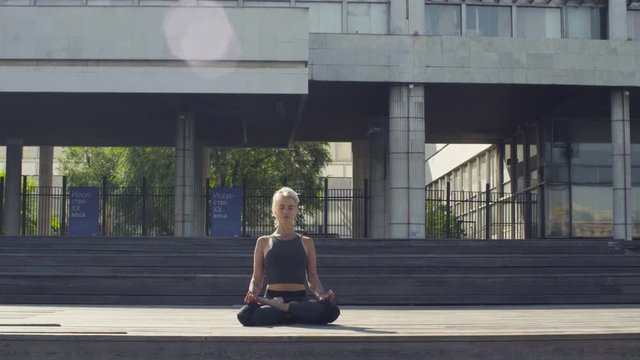 Young woman meditating against modern building