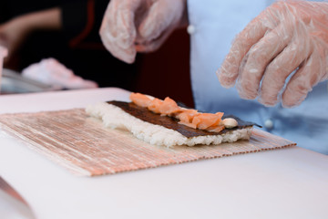 closeup hands rolling up sushi on bamboo mat - focus on the center of the sushi ingredients
