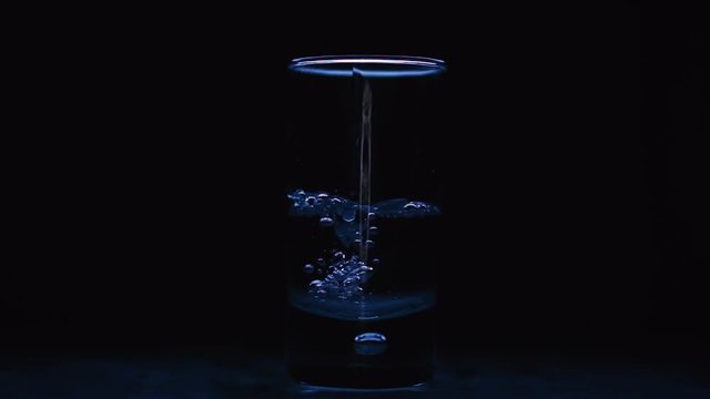 Water pouring into a glass, isolated black studio background