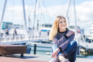 outdoor portrait of young happy smiling teen girl on marine background on a sunny day, auckland central wharf, new zealand