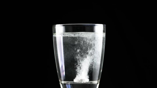 Effervescent antacid tablet in glass of water on black background with rotating
