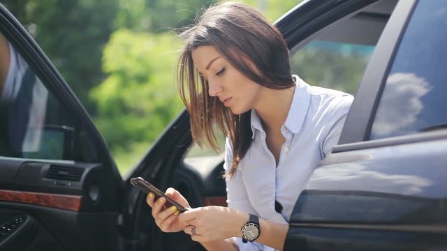Young woman using holding working mobile smart phone wireless modem lifestyle sitting car open doors communication traffic wristwatch watch attractive checking news online business trip sunny day