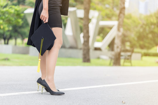 Back Of View Graduate Woman Holding Cap And Gown Walking On The Road