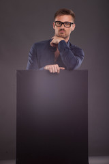 Young sexy man portrait of a confident businessman showing presentation, pointing paper placard black background. Ideal for banners, registration forms, presentation, landings, presenting concept.