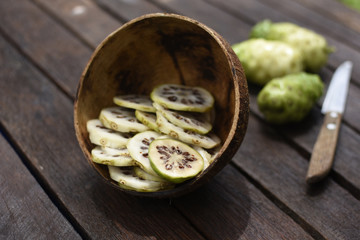 Noni slices in the coconut shell and noni fruit with knife on wooden table.Zoom in1