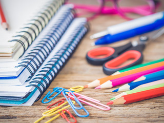Colorful school supplies with books, color pencils, pink glasses, pen cutter and clips on wooden background. Back to school concept.