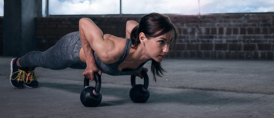 Young woman athlete in sportswear push ups with dumbbells