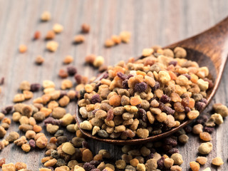 Closeup view of bee pollen in wooden spoon on brown wooden table