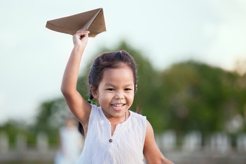 Cute asian child girl running and playing toy paper airplane in the field in vintage color tone