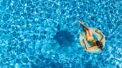 Aerial view of girl in swimming pool from above, kid swim on inflatable ring donut and has fun in water on family vacation
