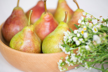 Pears in a wooden plate with white flowers on a light background