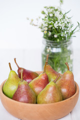 Pears in a wooden plate with white flowers on a light background