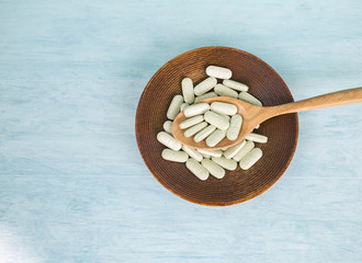 Pill food, green pill in wooden spoon on round wood plate with space on blue background
