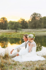 The bride and groom sit by the lake and look at the sunset