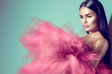 Gorgeous brunette model woman in pink dress posing in studio