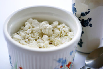 Food. Cottage cheese in a plate, a milk jug and a spoon on a table with a white tablecloth. Healthy food.