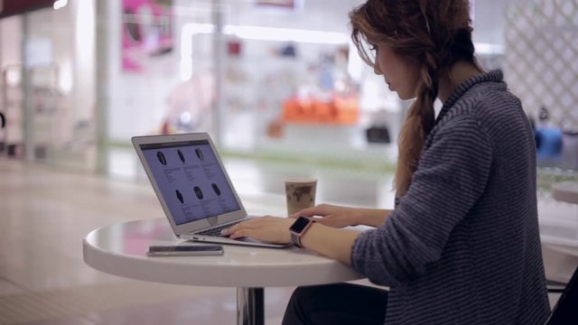 Young woman is looking in the online store for a new smart watch using a notebook