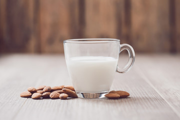 Glass of almond milk with almonds on wooden table