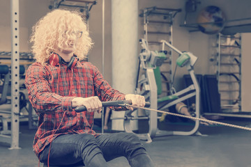Curly blonde guy in a red shirt and with glasses on training in the gym. Toned