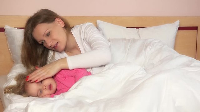 Mother caress her child girl lying in bed to make fall asleep.