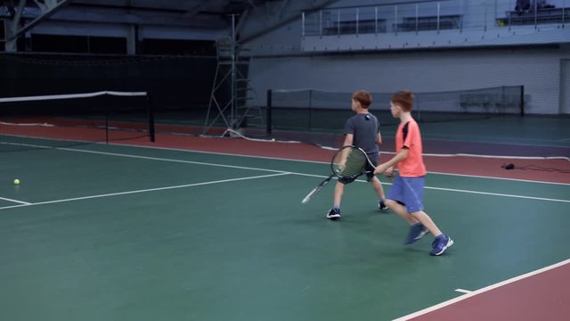Mother playing tennis with her sons at indoor court. Coach teaching boys playing professional sport game in recreation area. Young sportsmen learning returning and serving yellow balls with racket.