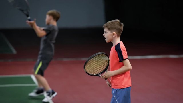 Two happy boys serving and returning balls on court with racket. Children hitting forehand in tennis having lesson. Young sportsmen learning playing sport game in recreation area.