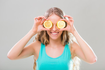 Beautiful woman covering eyes with slices of lemon on gray background.