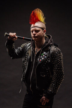 Portrait of punk rocker with Mohawk hairstyle holding baseball bat on a dark background.