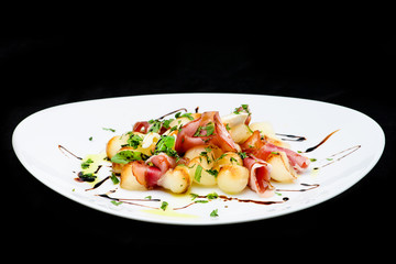 classic Italian summer delicious fresh salad with cheese, parma ham and soy sauce on white plate, on dark background, top view