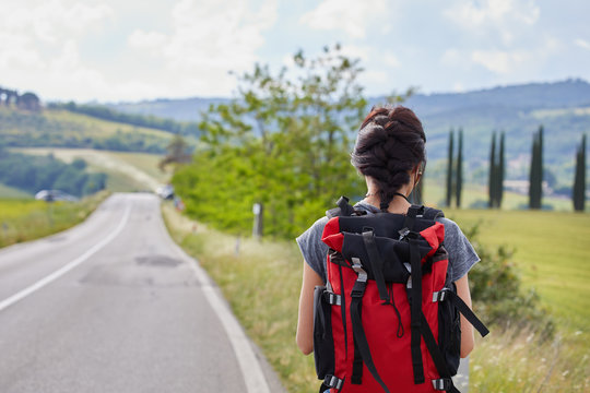 beautiful traveler woman carrying backpack walking on country road.