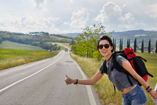 beautiful traveler woman carrying backpack walking on country road.