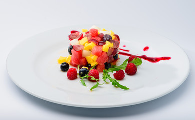 classic Italian food. Beautifully decorated fruit platter with blueberries, raspberries, watermelon, pineapple and plum with jam on a white plate, light background