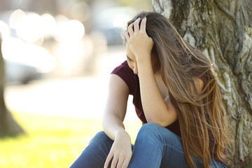 Fototapeta premium Sad woman lamenting sitting in a park
