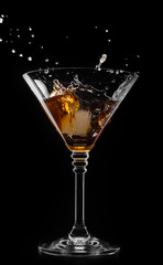 A glass with vermouth and ice cube on a black background