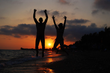 Fototapeta premium Couple jumping on beach at sunset. Happy people on the sea. Summer vacation concept