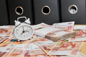 Time is money. An alarm clock and a lot of Russian money on the background of business folder