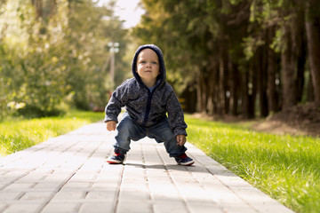 Funny baby boy squatting in the park. Autumn or summer shot